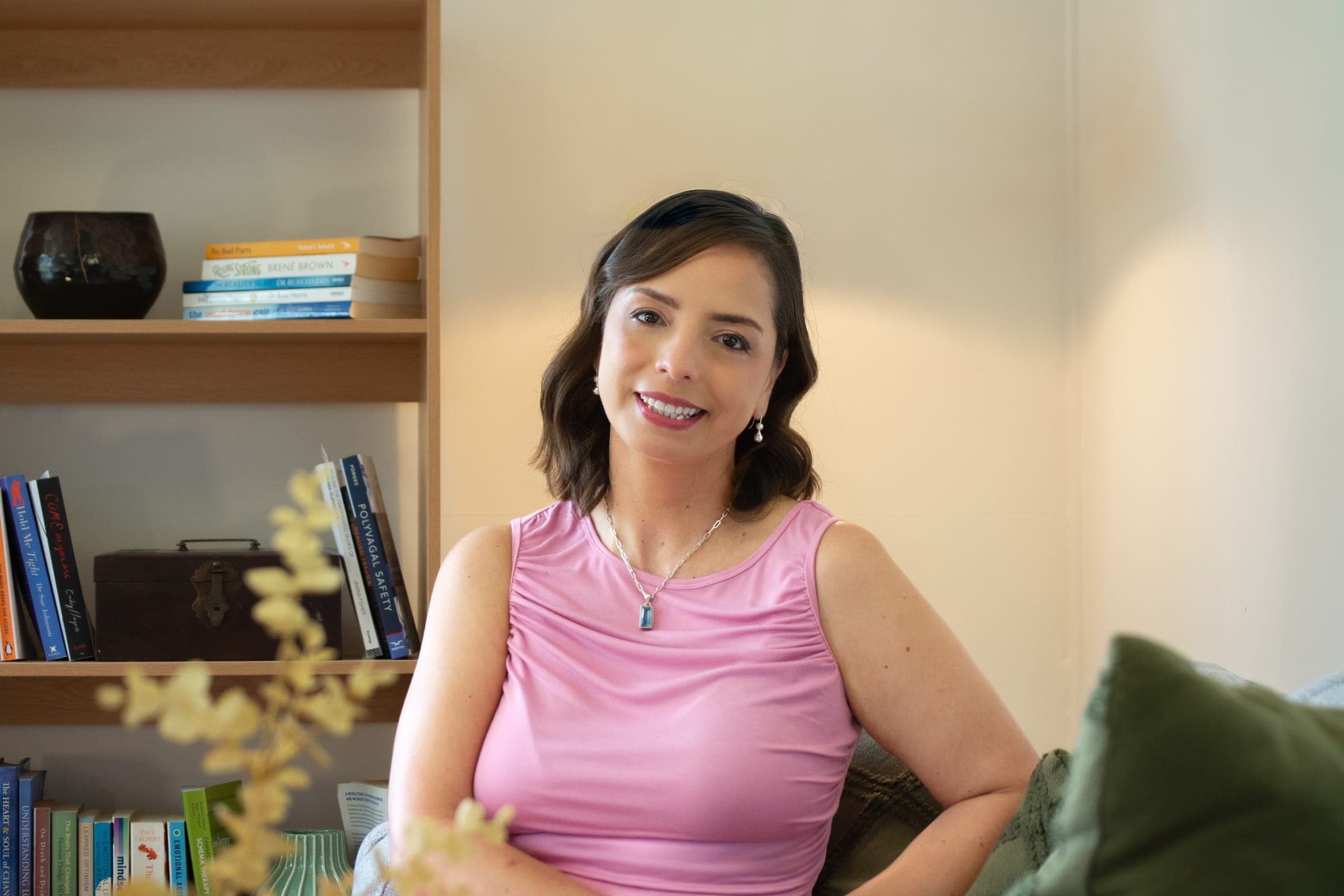 Alpha Ponce smiling, seated in her therapy room in front of a bookshelf