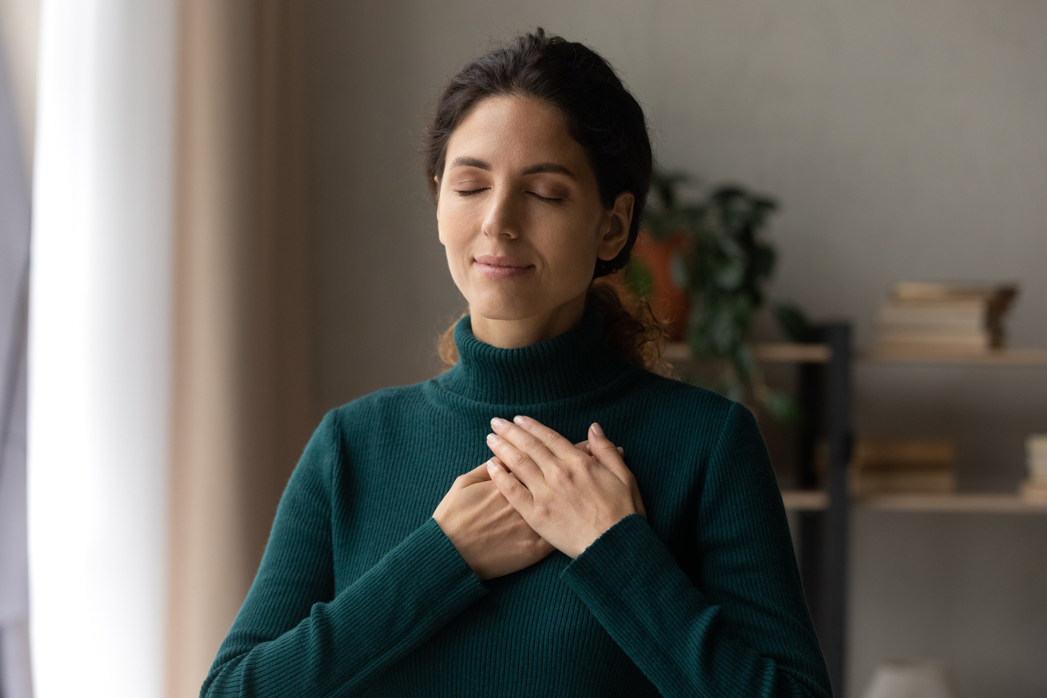 Peaceful young woman feeling thankful at home.